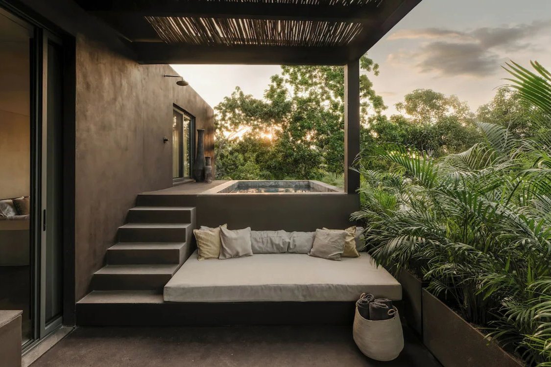 Terraza con daybed, pérgola y alberca privada en la selva, al atardecer