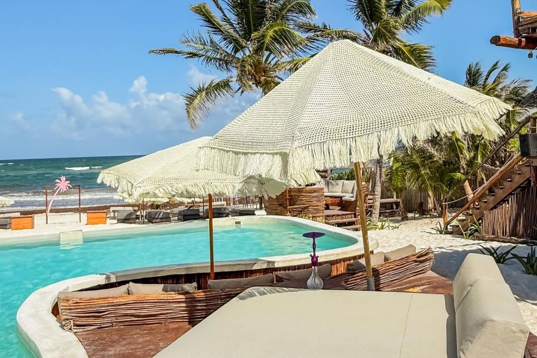 Alberca de Martina Beach Club frente al mar de Tulum, con sombrillas tejidas y camastros