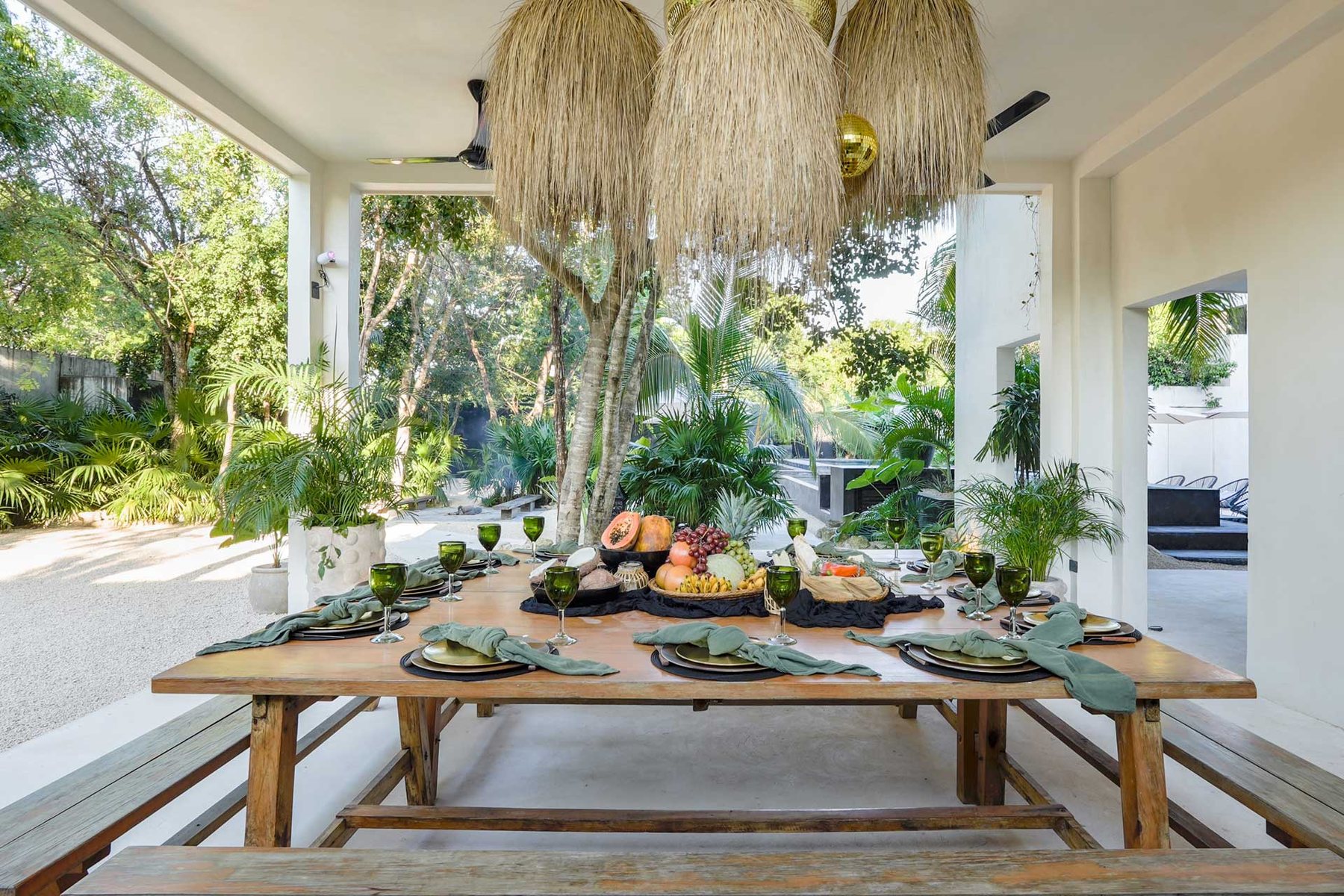 Mesa de comedor bajo lámparas de palma, abierta al jardín