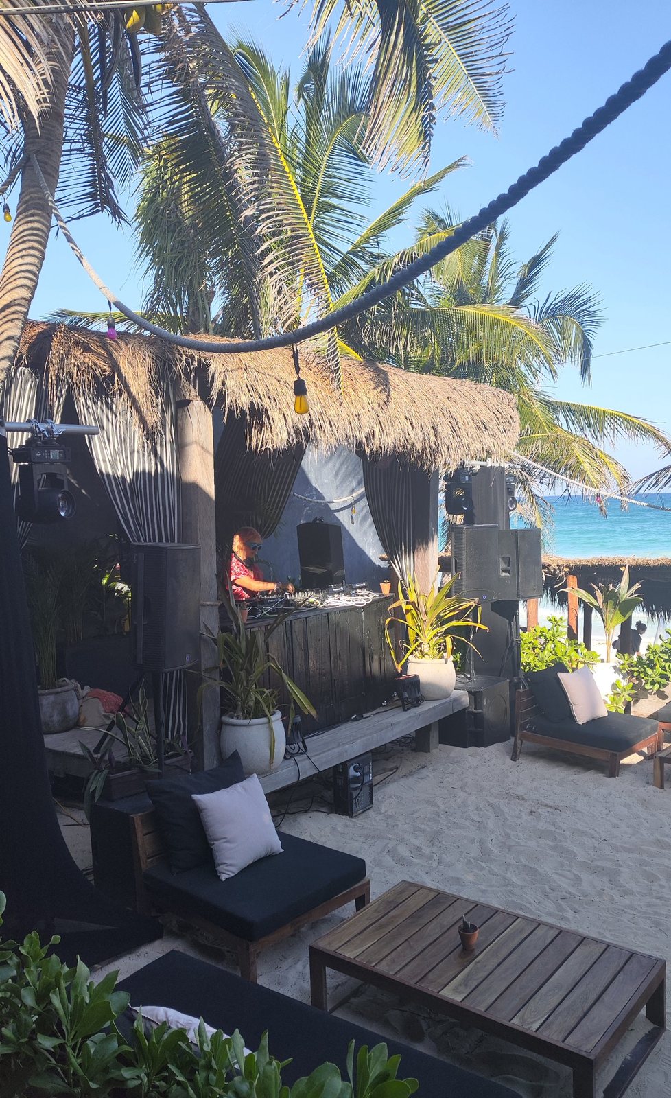 DJ en la cabina con bocinas a los lados, entre palmeras y frente al mar