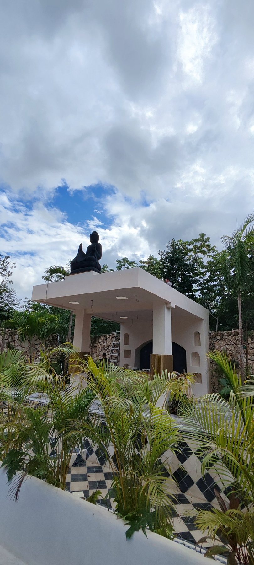 La pérgola con la escultura vista entre palmas
